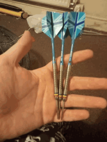 a hand holding three blue darts with a union jack design on them