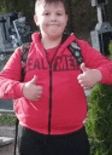 a young boy wearing a red jacket and giving a thumbs up .