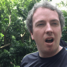 a man making a funny face with his mouth open in front of trees