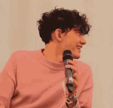 a young man in a pink sweater is holding a microphone and smiling