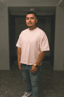 a man in a white t-shirt and blue jeans stands in a hallway