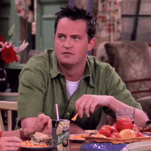 a man in a green shirt is sitting at a table eating food and drinking a can of johnny 's juice