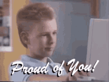 a young boy is sitting in front of a computer with the words proud of you written on the screen behind him .