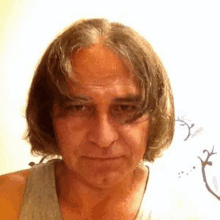 a man with long hair is wearing a gray tank top .