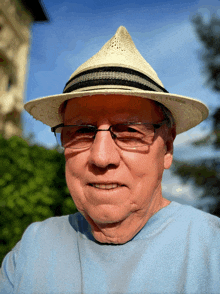 an older man wearing a hat and glasses smiles for the camera