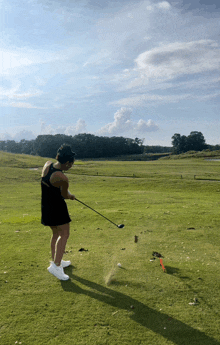 a woman in a black dress is swinging a golf club