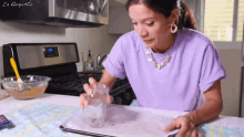 a woman in a purple shirt sits at a table in front of a stove with the word la doquette written on it