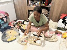 a woman sits on a messy bed with boxes of food and a box of candy