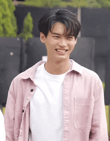 a young man wearing a white shirt and a pink shirt smiles