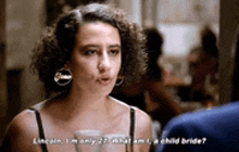 a woman with curly hair is talking to a man in a restaurant while wearing hoop earrings .