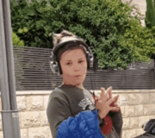 a young boy wearing headphones and a blue jacket stands in front of a fence