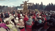 a large group of people are dancing in the snow with a scarecrow in the middle of the crowd .