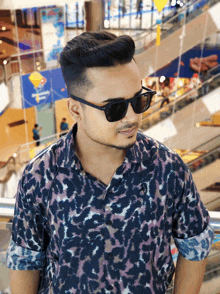 a man wearing sunglasses stands in front of an escalator in a mall