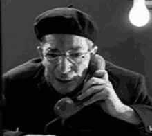 a man wearing glasses and a beret is talking on a phone .