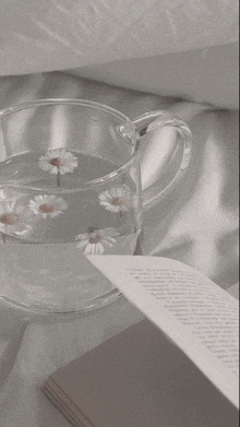 a cup of water with daisies floating in it next to a book