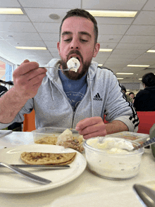 a man wearing an adidas sweatshirt eats food