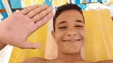 a young boy is smiling and waving at the camera while laying on a beach towel .