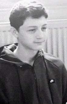 a black and white photo of a young man wearing a nike jacket .