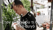 a man in a black shirt is standing in front of some plants with a foreign language written on the bottom