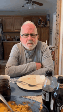 an elderly man sits at a table with a plate of food and a bottle of coke