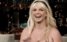 britney spears is laughing while sitting on a couch wearing a bikini top .