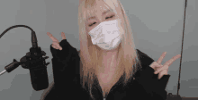 a blonde woman wearing a face mask giving a peace sign