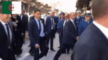 a group of men in suits and ties are walking down a street with the flag of algeria behind them