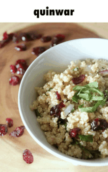 a bowl of quinoa with cranberries and parsley on a wooden cutting board