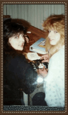 two women are sitting at a table with a book in the background