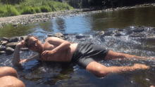 a shirtless man is laying in a river with his legs in the water .