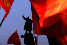 a statue of a man is surrounded by red flags and one of them has the letter o on it