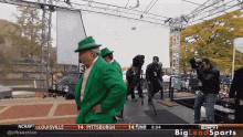 a man in a green suit and hat stands on a stage in front of a sign that says ncaaf on it