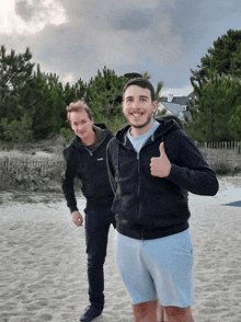 a man giving a thumbs up while standing on a sandy beach