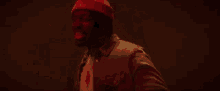 a man wearing a red hat and a white shirt is standing in a dark room in a red light .