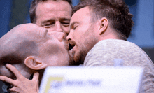 a man is kissing another man 's face in front of a sign that says f