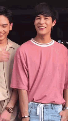 a man in a pink shirt is smiling while standing next to another man .