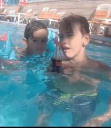 two young boys in a swimming pool with a bottle of coca cola