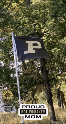 a proud boilermaker mom flag is flying in front of a tree