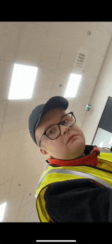 a man wearing glasses and a yellow vest is taking a picture of himself .