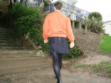 a person wearing a black skirt and an orange sweater is walking down a set of stairs