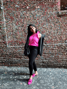 a woman in a pink top and black jeans stands in front of a wall covered in chewing gum