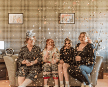 four women are sitting on a couch with confetti flying around them