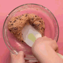 a person is mixing a cookie dough in a glass bowl with mr.cakes written on the bottom of the bowl