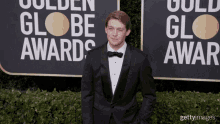 a man in a tuxedo stands on a red carpet in front of a sign that says golden globe awards