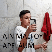 a young man taking a selfie in front of a wall that says " ain malfoy apelaum " on it