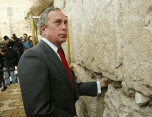 a man in a suit and red tie stands in front of a wall