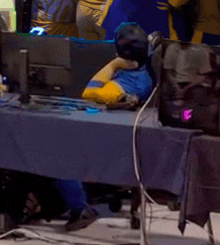 a man in a blue and yellow shirt sits in front of a computer