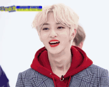 a young man with blonde hair wearing a red hoodie and a plaid jacket