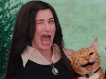 a woman is holding a smiling cat in her arms and making a funny face .