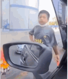 a young boy wearing a mask is standing in front of a car looking in the rear view mirror .